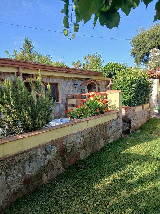 Stone house with well-kept garden, flower beds and rustic wall in a green and sunny environment.