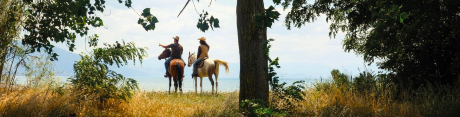 Coppia a cavallo che ammira il panorama naturale circostante.
