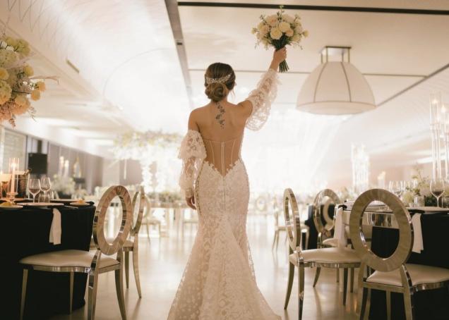 Braut in einem Spitzen-Meerjungfrauenkleid mit einem Blumenstrauß bei einem eleganten Hochzeitsempfang.