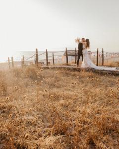 Das Brautpaar küsst sich auf einem Holzsteg über dem Meer bei Paestum, umgeben von goldenem Gras und dem warmen Licht des Sonnenuntergangs.