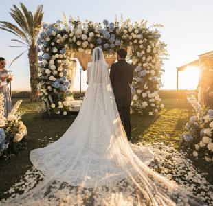 Hochzeit im Freien bei Sonnenuntergang mit Braut und Bräutigam unter einem weiß-blauen Blumenbogen.