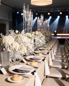 Elegante Eventdekoration mit einer langen imperialen Tafel, weißen Blumen, Kerzenleuchtern aus Glas und stilvollen Sitzgelegenheiten.