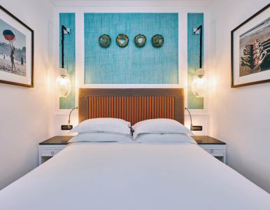 Elegant bedroom with double bed, decorative orange and blue striped headboard, turquoise wall, bright wall lamps and refined design details.