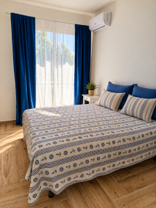 Helles Schlafzimmer mit Doppelbett, blauen und weißen Vorhängen und Bettwäsche im maritimen Stil.