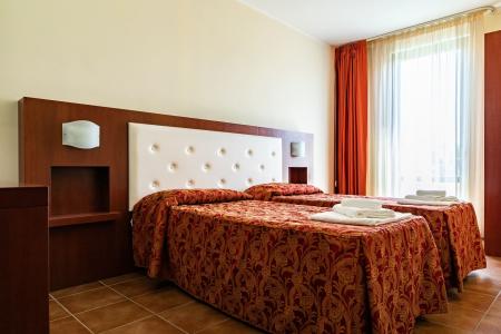 Hotel bedroom with two single beds, patterned bedding, an upholstered headboard, and orange curtains.