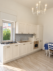 Helle und moderne Küche mit weißen Möbeln, Kochfeld, Backofen, Spüle und Esstisch.