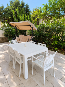 Weiße Gartenmöbel mit Tisch und Stühlen, Schaukel und grünen Pflanzen auf einer Außenterrasse.