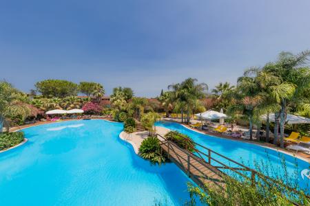 Resort's panoramic swimming pool with turquoise water, palm trees, sun loungers, and parasols nestled in lush greenery.