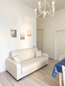 Helles Wohnzimmer mit weißem Sofa, elegantem Kronleuchter, Esstisch und Möbeln in neutralen Farbtönen.