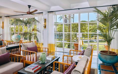 Bright, tropical-style veranda with bamboo furnishings, ornamental plants and large windows overlooking the garden.
