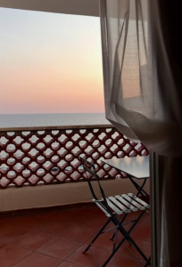 Balcon avec vue sur la mer au coucher du soleil, avec une table et des chaises donnant sur l’horizon.