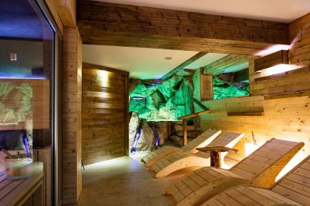 Wooden relaxation area with a chaise longue and an illuminated stone wall.